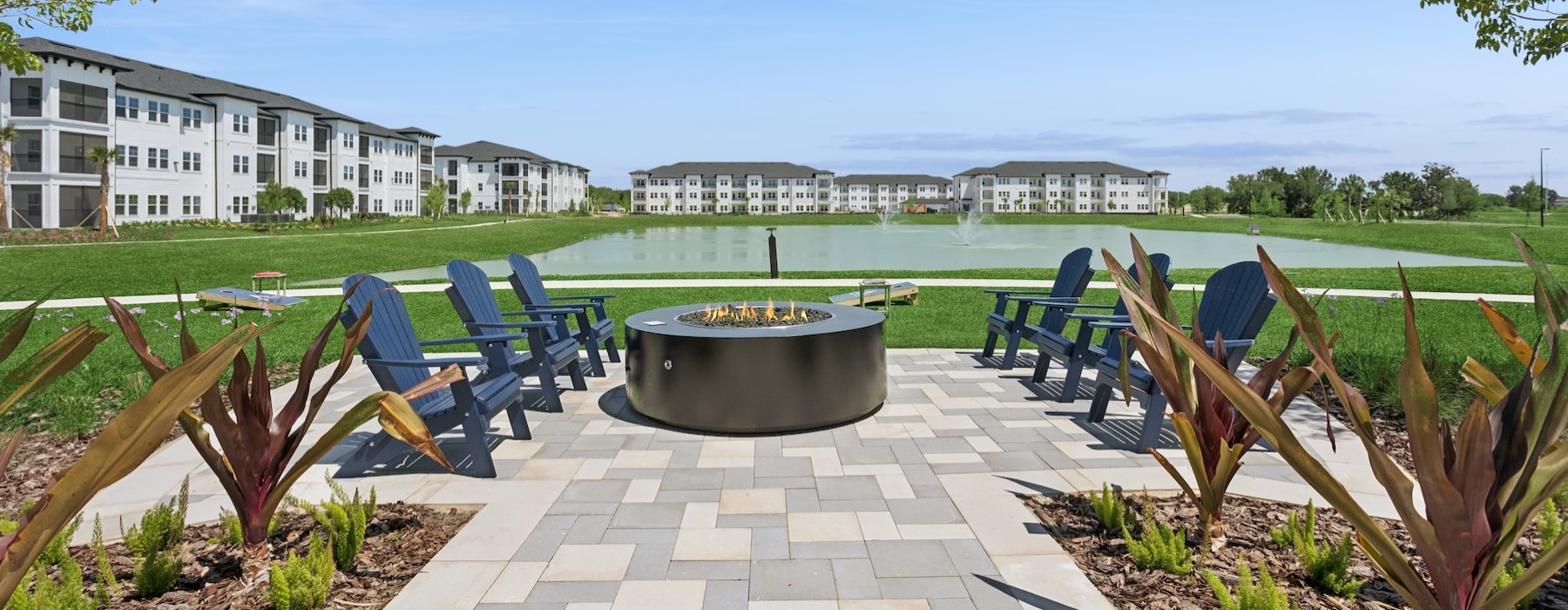 a patio with chairs and a firepit by a body of water